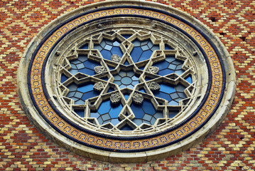 Beautiful facades of religious buildings: a close-up photo of a rose window on a patterned brick wall. Exterior detail of the Cetate Synagogue in the Old Town of Timisoara (Timiș County, Romania)