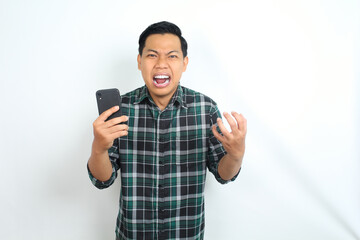 Fototapeta premium furious asian man shouting while holding cellphone and raising his hand show angry face isolated on white background