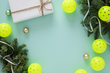 Flatlay with Christmas pickleball decorative border with balls, ornaments, pine branches, gift box and ribbon. Horizontal orientation with copy space.