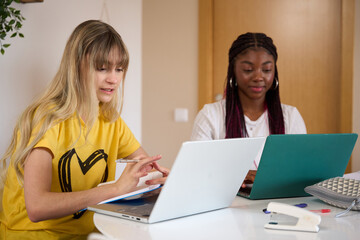 Multiethnic students studying together with laptops and notebooks at home