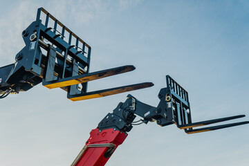 Two construction telehandler fork attachments raised as lifts up in the air