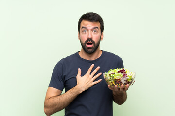 Young handsome man with salad over isolated green wall surprised and shocked while looking right