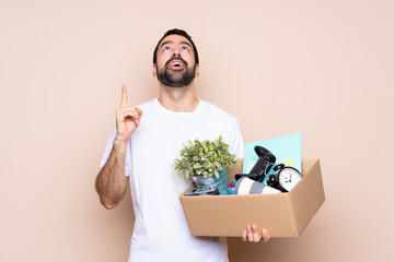 Man holding a box and moving in new home over isolated background pointing up and surprised