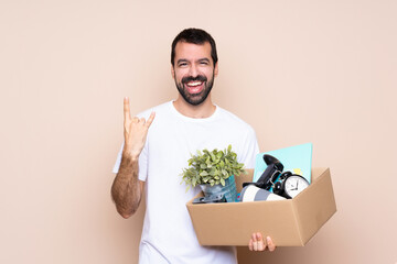 Man holding a box and moving in new home over isolated background making rock gesture