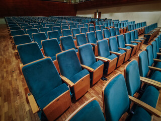 Fototapeta premium Rows of empty blue upholstered seats with wooden armrests in an auditorium. The warm wooden flooring and soft lighting create a cozy atmosphere.