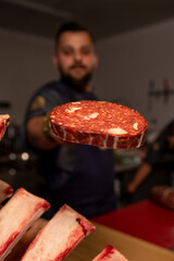 Butcher displaying freshly cut sausage slices to the camera in a butcher shop. Cook cuts pieces of homemade meat products.