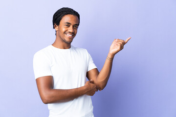 Young African American man with braids man isolated on purple background pointing finger to the side