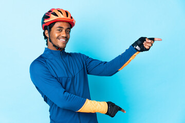 Young cyclist man with braids over isolated background pointing finger to the side and presenting a product