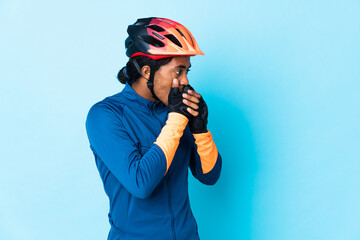 Young cyclist man with braids over isolated background covering mouth and looking to the side
