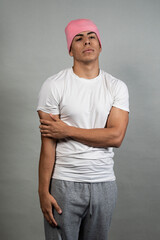 Young latin man wearing pink beanie, white t-shirt and gray sweatpants is posing with crossed arms