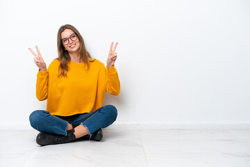 Young caucasian woman sitting on the floor isolated on white background showing victory sign with...