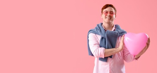 Happy young man holding heart-shaped balloon on pink background with space for text. Valentine's Day celebration