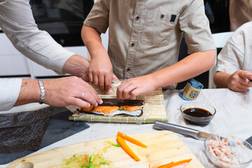Hands of a family making homemade sushi