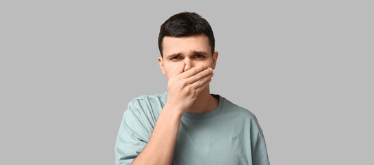 Young man feeling bad smell on grey background