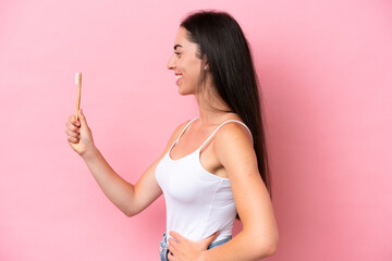 Young caucasian woman brushing teeth isolated on pink background with happy expression