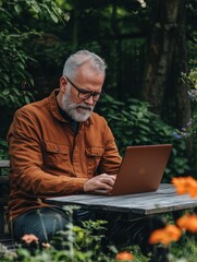 Mature man with laptop and smartphone working outdoors in garden, home office concept.