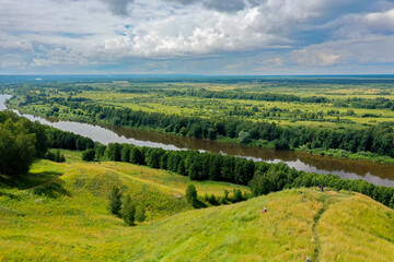 Majestic Klyazma River flows serenely through verdant hills in Gorokhovets, set against a backdrop of fluffy clouds.