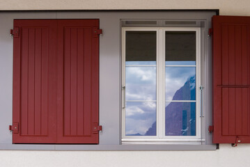 Fototapeta premium Vintage Windows with flowers and shutters in Switzerland. The Windows reflect the beautiful views of the mountain peaks
