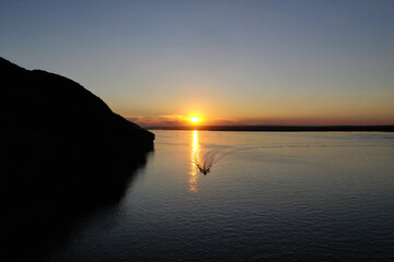 Fototapeta premium A serene sunset paints the Vilga river with golden light, creating a peaceful atmosphere at evenings edge.