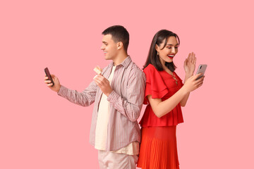 Young couple with mobile phones and engagement ring on pink background. Online dating