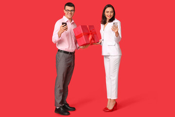 Young couple with mobile phones and gift box on red background. Online dating