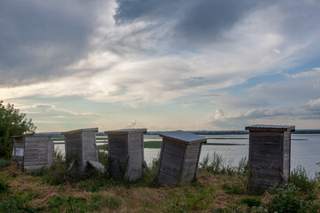 Beehives stand weathered by time near the tranquil waters of Sviyazhsk, illuminated by the soft glow of dusk.