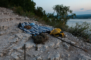 Camping gear rests on a rocky outcrop, capturing the tranquility of twilight by the riverside.