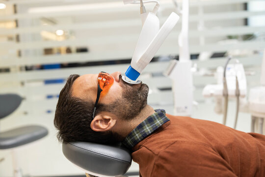 Patient in a dental chair from a side angle, with a dental lamp positioned above, showcasing the equipment used in dental treatments for whitening teeth