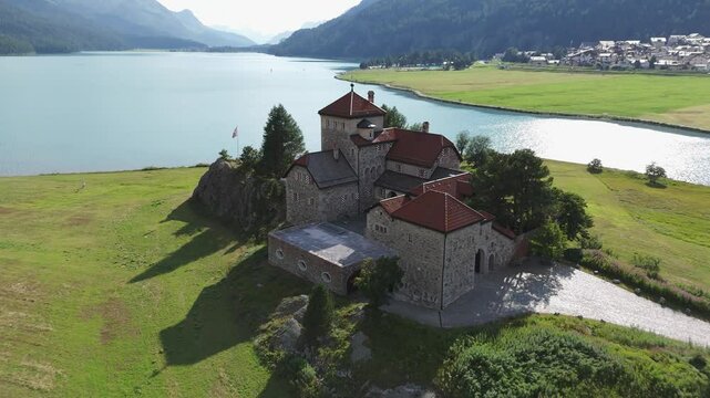 Aerial view pull back reveal of historic castle overlooking Lake Silvaplana, St. Moritz, Grisons Canton, Maloja Region, Switzerland. 
