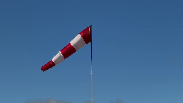 Red and white windsock on a metal pole against a clear blue sky, indicating wind direction and speed