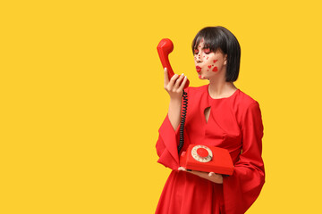 Beautiful young woman with creative makeup for Valentines Day and retro telephone on yellow background