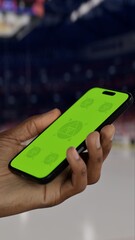GREEN SCREEN CHROMA KEY A hand holding a phone with a green screen at a hockey game in an indoor stadium, ideal for showcasing live sports or betting apps