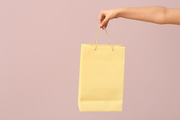 Female hand with paper shopping bag on light background. Valentine's Day celebration