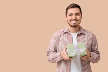 Young man with gift box on beige background. International Women's Day