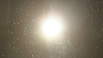 Many dust particles floating falling in light on empty background with bright spotlight from above.