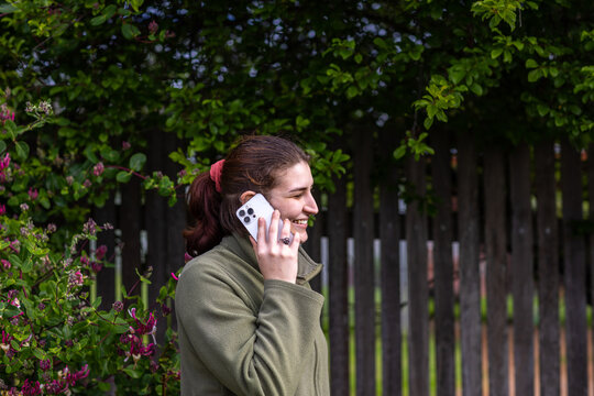 young woman outside in front of foliage near picket fence with phone to ear
