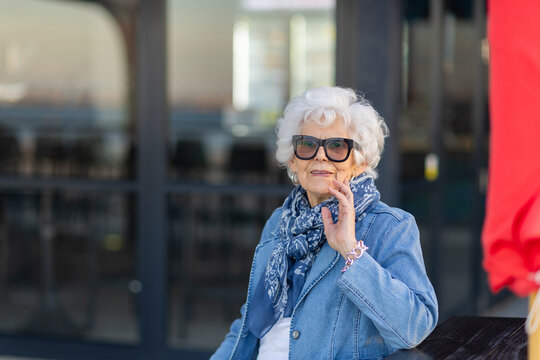 elderly lady wearing sunglasses with denim sitting with hand to face