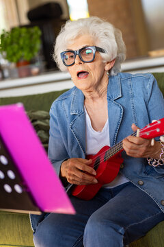 elderly lady wearing thick-rimmed glasses singing and playing ukulele