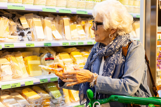 elderly lady choosing cheese from a large variety at a supermarket
