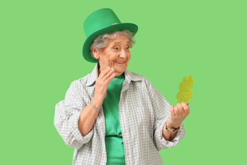 Surprised senior woman in leprechaun hat with paper clover for St. Patrick's Day celebration on...