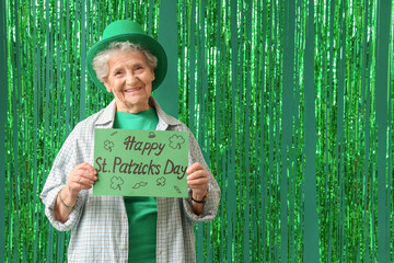 Senior woman in leprechaun hat holding festive postcard with text HAPPY ST. PATRICK'S DAY on green...