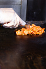 A gloved chef grills seasoned chicken pieces on a flat-top grill, highlighting professional fast food preparation.
