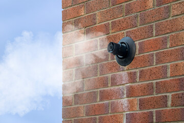 Condensing Gas Boiler Flue Steam Vapor Emitted from Black Pipe on Red Brick Wall against Blue Sky