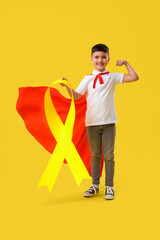 Little boy dressed as superhero with gold ribbon showing muscles on color background. Childhood cancer awareness concept