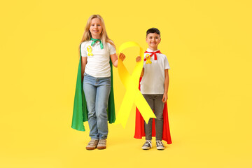 Fototapeta premium Little children dressed as superheroes with gold ribbons on color background. Childhood cancer awareness concept