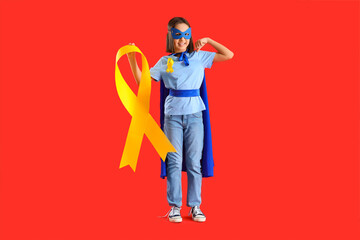 Fototapeta premium Little girl dressed as superhero with gold ribbon showing muscles on red background. Childhood cancer awareness concept