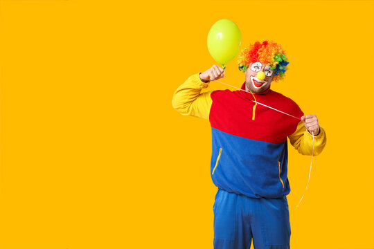 Young man as bad clown showing strangulation with balloon on yellow background