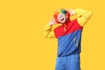 Obraz premium Young man as crazy clown in headphones laughing on yellow background