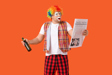 Young man as shocked alcoholic clown with bottle of beer and newspaper on orange background