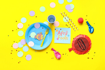 Table setting with whoopee cushion, festive postcard and decor for April Fools Day on yellow background